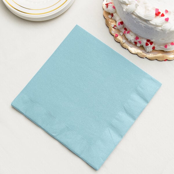 A Pastel Blue Creative Converting paper dinner napkin on a stack of plates with a white cake.