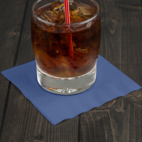 A glass of ice tea with a straw on a navy blue Creative Converting beverage napkin.