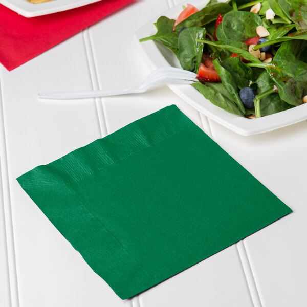 A Creative Converting emerald green luncheon napkin with a fork next to a bowl of salad.