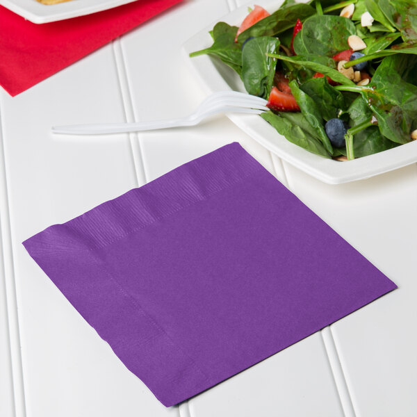 A purple Creative Converting luncheon napkin next to a plate of salad.