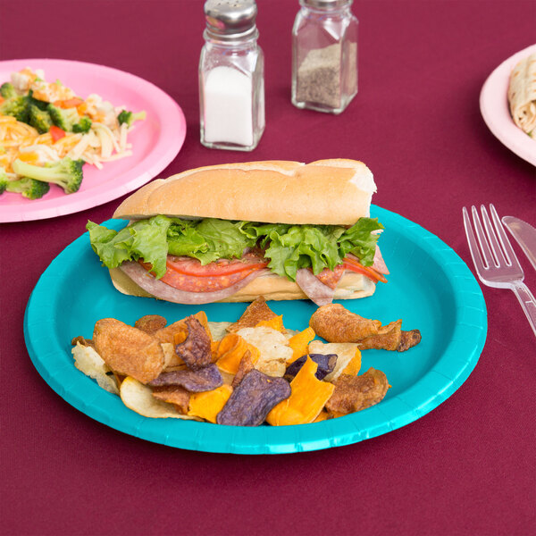 A Bermuda Blue paper plate with a sandwich, lettuce, tomato, and meat on a table.