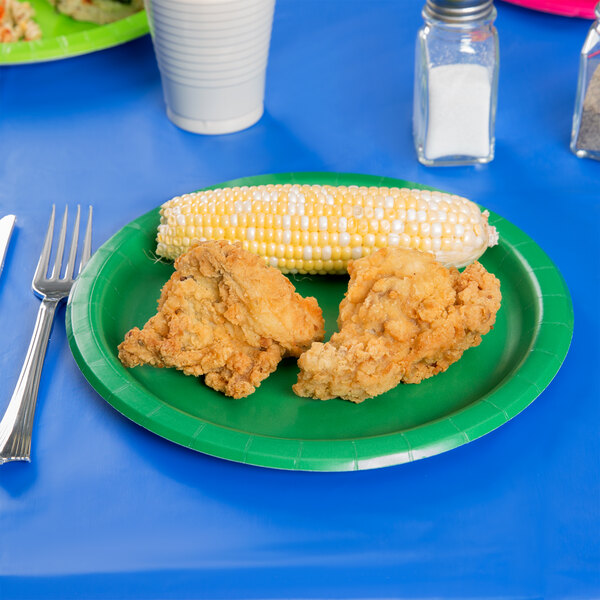 A plate of fried chicken and corn on the cob on an emerald green paper plate.