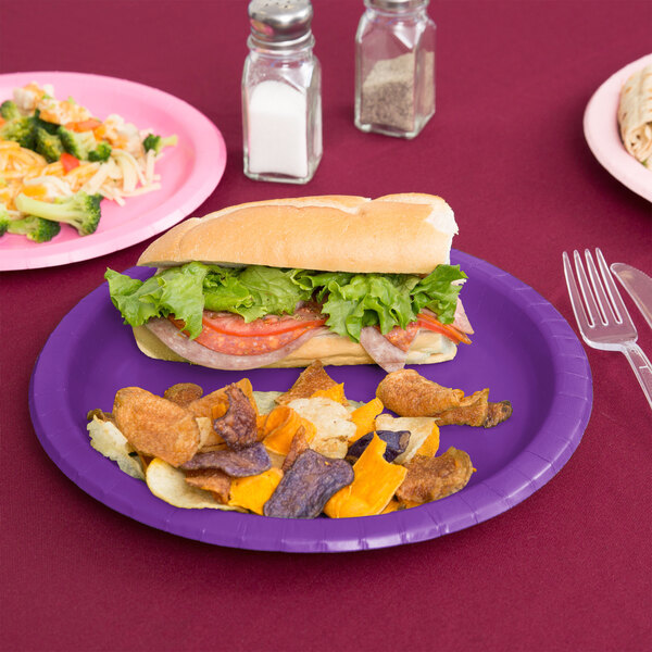 A sandwich on an amethyst purple paper plate with chips.