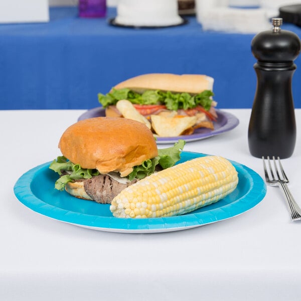 A Creative Converting turquoise blue paper plate with a sandwich and corn on the cob on a table.