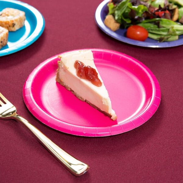 A slice of cheesecake on a Creative Converting hot magenta pink paper plate next to a fork.