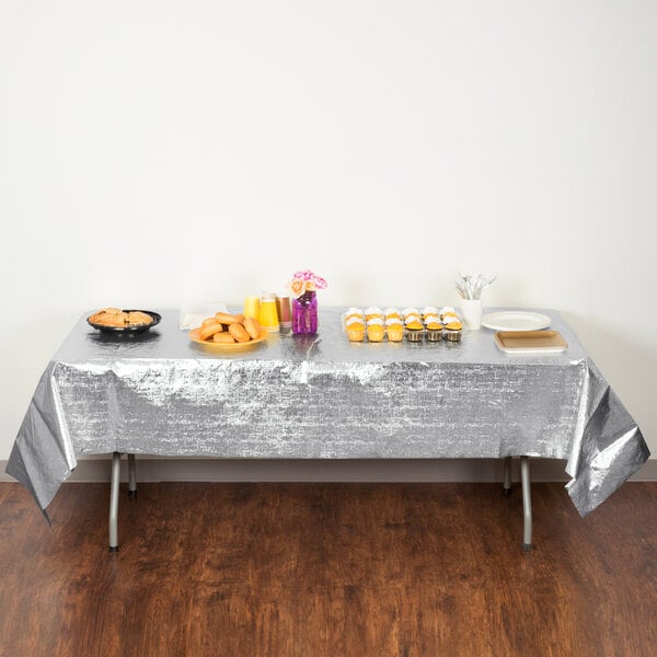 A silver Creative Converting plastic table cover on a table with food.