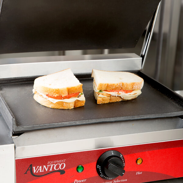 An Avantco flat bottom grill cooking a sandwich with cheese, meat, and tomato.
