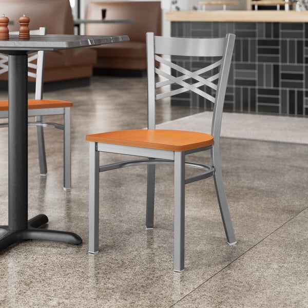 A Lancaster Table & Seating cross back chair with a cherry wood seat at a table in a restaurant.