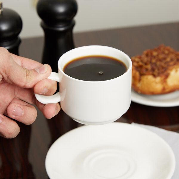 A person holding an Arcoroc Daring porcelain cup of coffee over a plate of donuts.