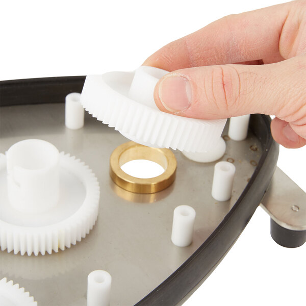 A hand holding a white plastic gear bearing.