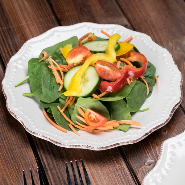 A 10 Strawberry Street Oxford brown rim stoneware salad plate with a salad of spinach, carrots, and peppers on a table.