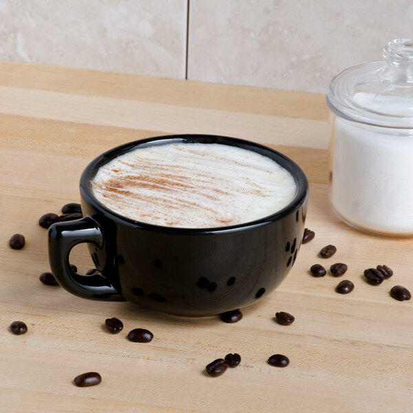 A black Tuxton jumbo cappuccino cup with white liquid and brown beans.