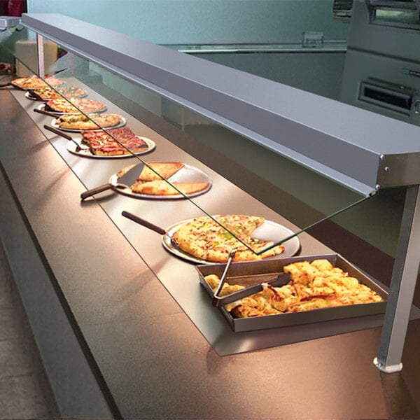 A Hatco heated shelf built into a counter with a row of pizzas on plates.