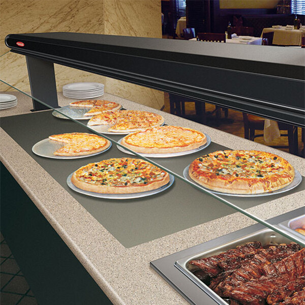 A Hatco heated shelf with pizzas on plates on a hotel counter.