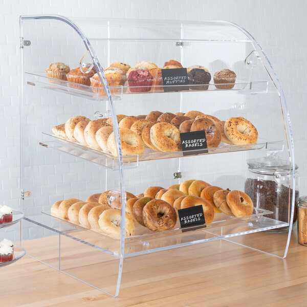 A Vollrath clear acrylic bakery display case with bagels, donuts, and cupcakes.