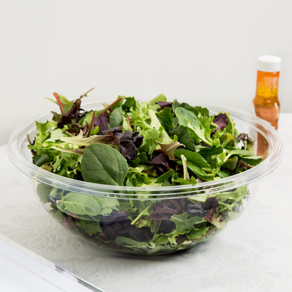 A bowl of salad with green leaves in a clear plastic bowl.