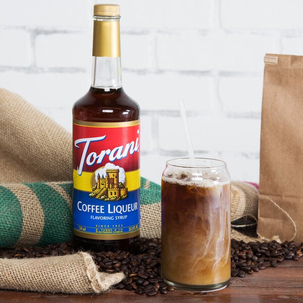 A Torani coffee liqueur flavoring syrup bottle next to a glass of coffee flavored liquid.