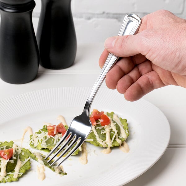A hand holding a Libbey stainless steel dinner fork over a plate of food.