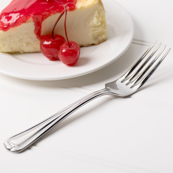 A Libbey stainless steel utility fork with a slice of cheesecake on a plate.