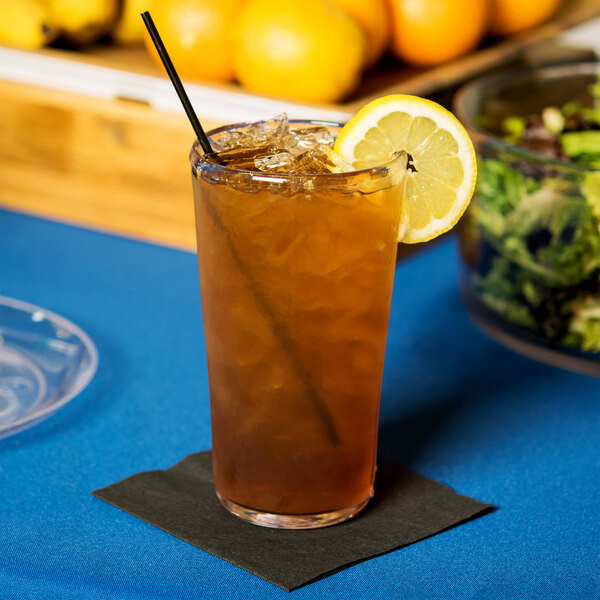 A Carlisle clear plastic cooler glass filled with iced tea and topped with a lemon wedge on a blue table.