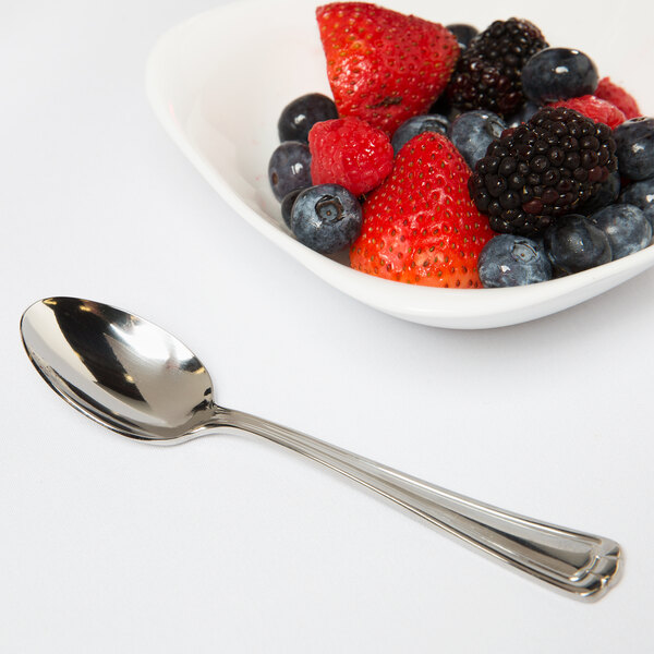 A bowl of berries and a Libbey stainless steel teaspoon on a white surface.