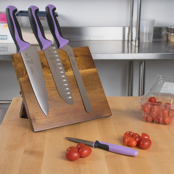 A Mercer Culinary Millennia knife set with purple handles on an acacia magnetic board.