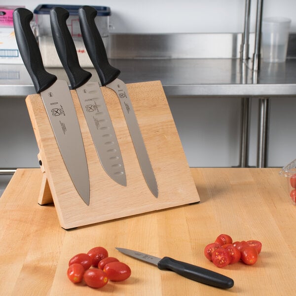 A Mercer Culinary Millennia® knife set on a Mercer Culinary rubberwood magnetic board with black handles.