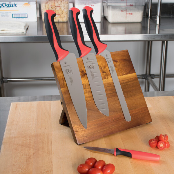 A Mercer Culinary Millennia Colors knife set with red handles on a wooden cutting board with tomatoes.