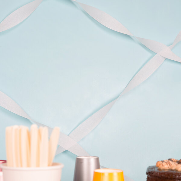 A table with a white cake and silver cups with white streamers on the wall.