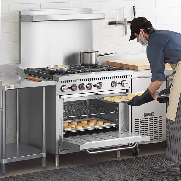 A man in a professional kitchen using a Cooking Performance Group 6 burner range with an oven to cook food.