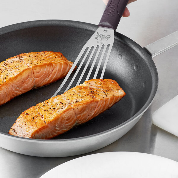 A pan with two salmon steaks being cooked with a Mercer Culinary Hell's Handle fish turner.