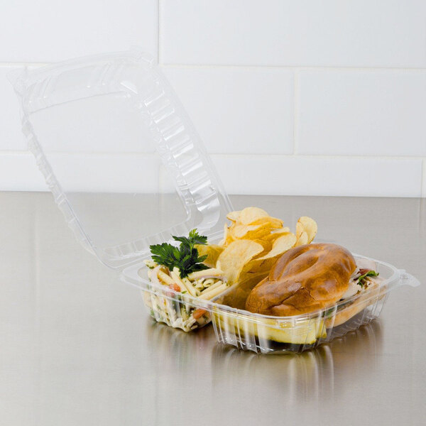A Dart clear hinged plastic container with food inside and a bowl of chips.
