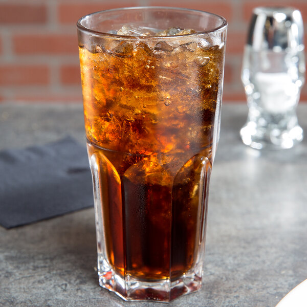 An Arcoroc stackable beverage glass filled with cola and ice sits on a table.