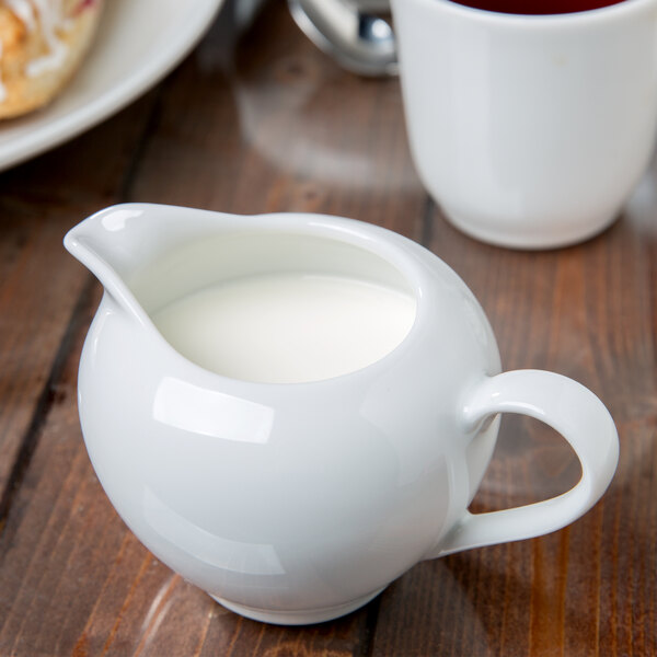 A white 10 Strawberry Street porcelain creamer filled with milk next to a cup of tea.