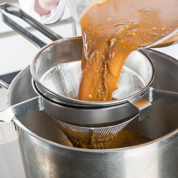 A person using a Vollrath fine china cap strainer to pour brown liquid into a pot.