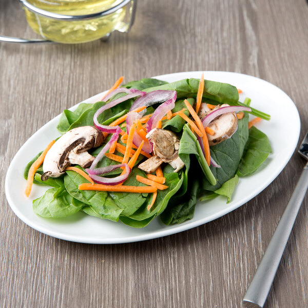 A 10 Strawberry Street white porcelain oval salad plate with a salad of spinach, mushrooms, and carrots on it.