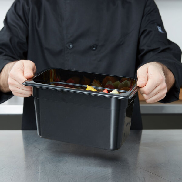 A chef holding a Cambro black plastic food pan filled with fruit.