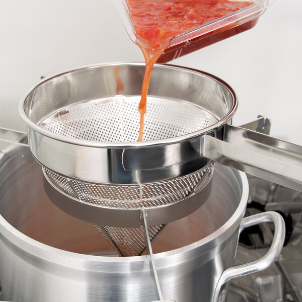 A person using a Vollrath Coarse China Cap Strainer to pour sauce into a pot.