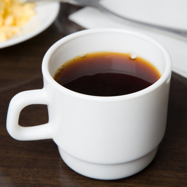 An Arc Cardinal stackable mug filled with brown liquid on a table with a plate of food.