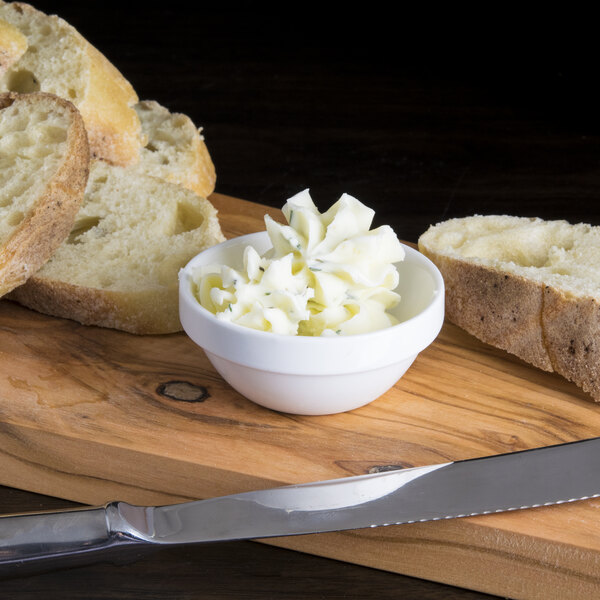 A stackable bowl of butter next to a knife on a wood surface.
