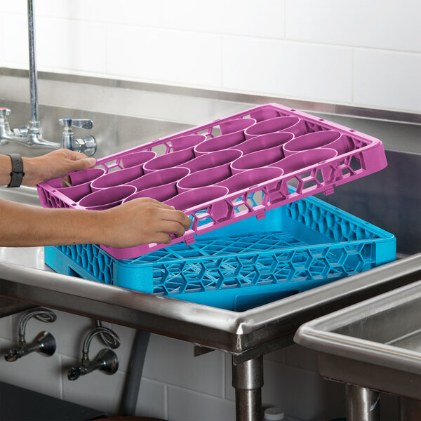 A person holding a purple and blue Carlisle OptiClean glass rack.