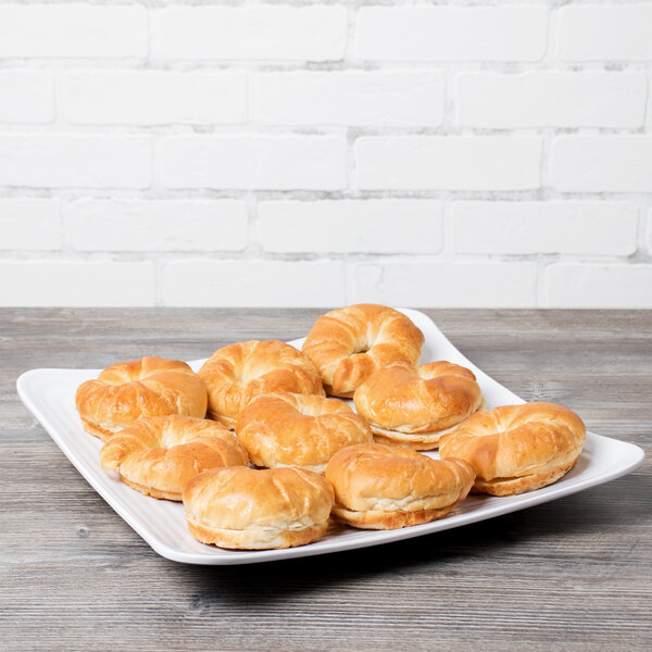 A white Milano melamine square plate with a variety of pastries on a wood table.
