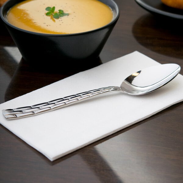 A 10 Strawberry Street Panther Link stainless steel dinner spoon on a napkin next to a bowl of soup.