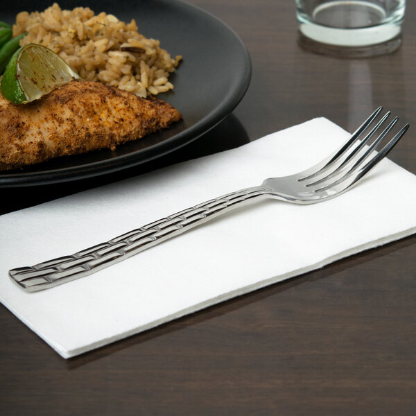 A 10 Strawberry Street Panther Link stainless steel dinner fork on a white napkin next to a plate of food.