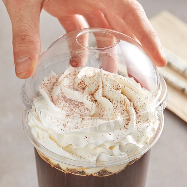 A hand holding a Choice clear plastic cup with a dome lid filled with a drink and whipped cream.