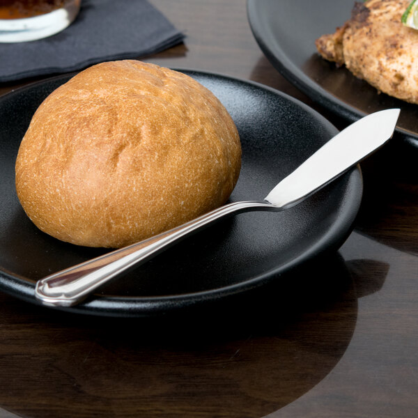 A black plate with a piece of round brown bread and a 10 Strawberry Street stainless steel butter knife.