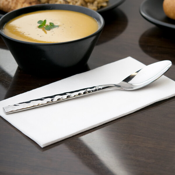 A silver 10 Strawberry Street heavy weight stainless steel dinner spoon in a bowl of soup on a table.