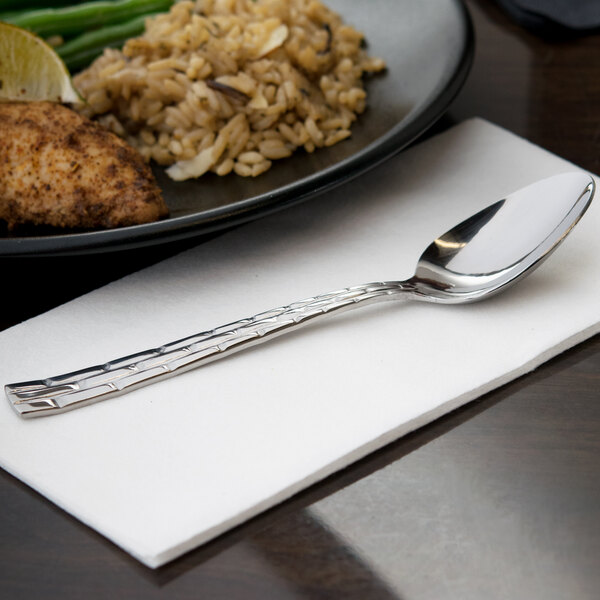 A 10 Strawberry Street Panther Link stainless steel teaspoon on a napkin next to a plate of food.