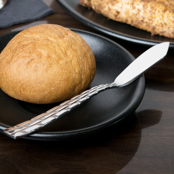 A black plate with a piece of round brown bread and a Panther Link stainless steel butter knife.