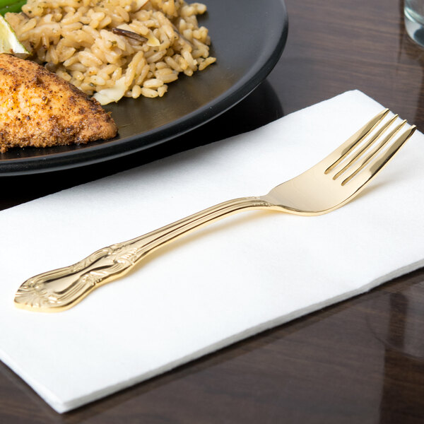 A 10 Strawberry Street Crown Royal gold plated stainless steel salad fork on a napkin next to a plate of food.